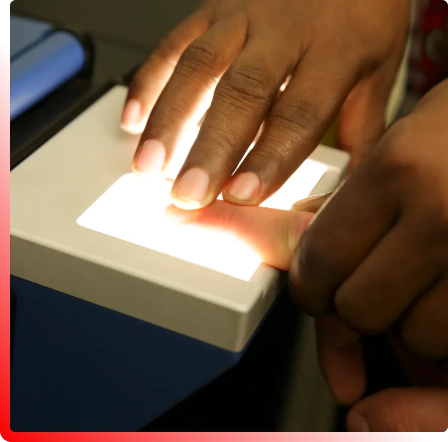 A person's fingers are being placed on a fingerprint scanner, illuminated by bright light.